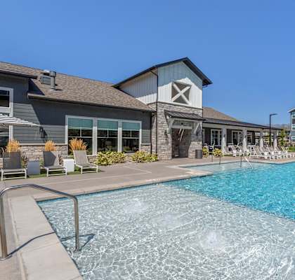 A swimming pool in front of a building with a stone wall and patio furniture.