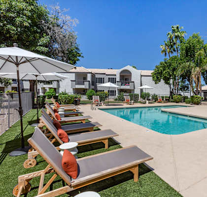 a pool with lounge chairs and umbrellas in front of a building