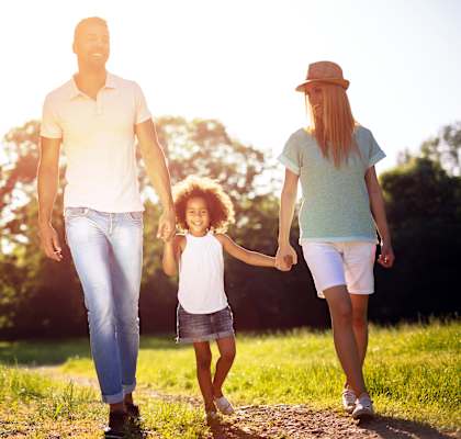 A family of three is walking hand in hand through a grassy path.at Villa Solera, San Jose, CA