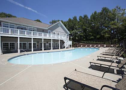 A large swimming pool is surrounded by sun loungers and a building with a balcony.