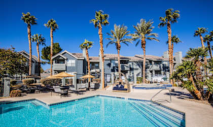 A swimming pool surrounded by palm trees and lounge chairs.