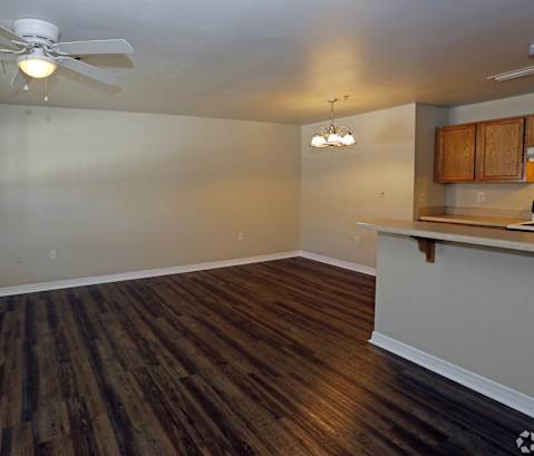 an empty living room with a kitchen and a ceiling fan