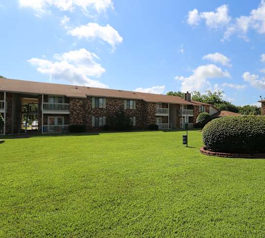 A grassy courtyard in front of a building with a bush in the middle.