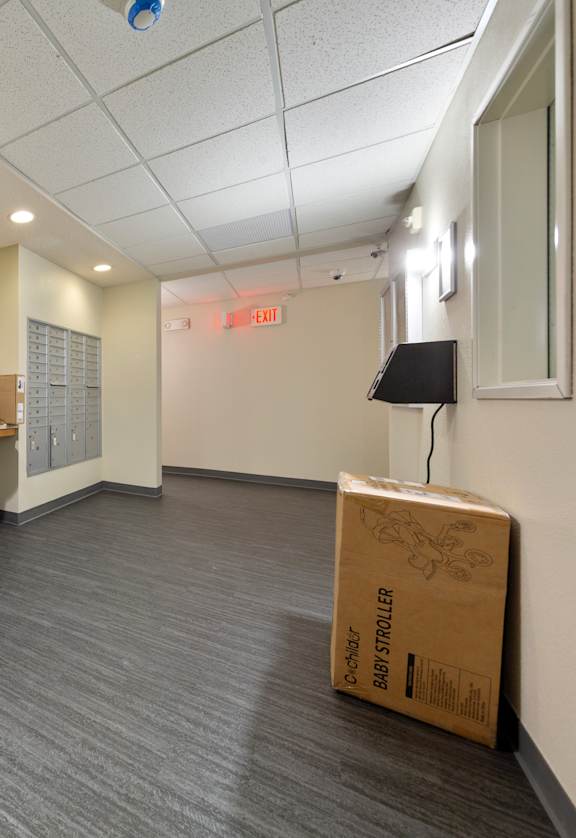 A cardboard box with the word "STRUCTURE" on it is sitting on the floor of a room with a row of mailboxes on the wall.