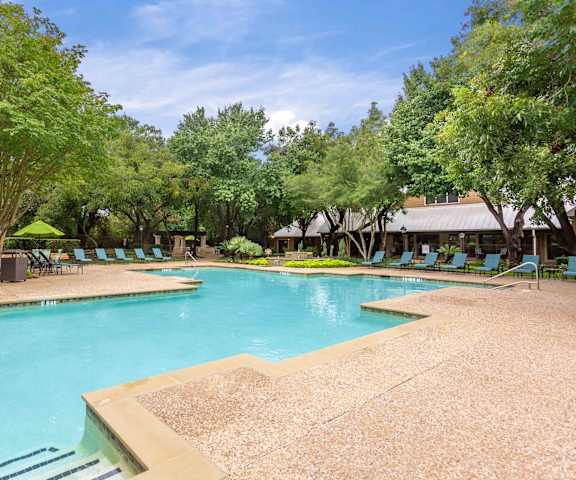 A large swimming pool surrounded by trees and lounge chairs at Ventana Oaks Apartments, Texas
