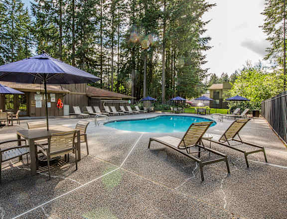 A pool area with a blue umbrella and lounge chairs.