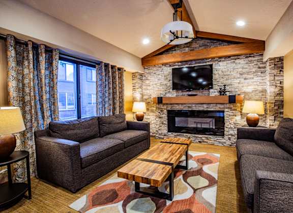 A living room with a stone fireplace and a flat screen TV mounted above it.