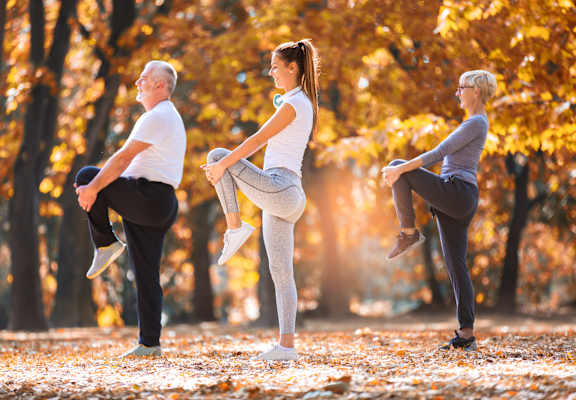 Three people doing stretching exercises in a park.