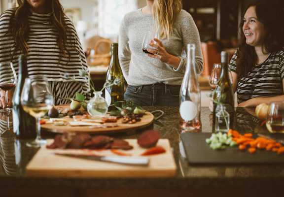 a group of women standing around a table with food and drinks