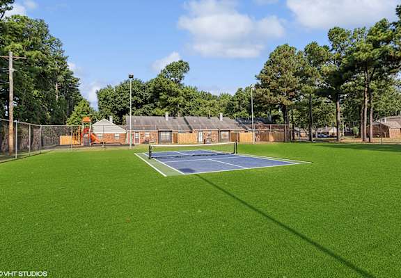 a tennis court with a blue court in the middle of a grass field at The Birches Apartment Homes, Memphis, TN