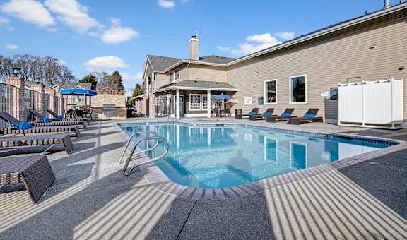 A large outdoor swimming pool surrounded by lounge chairs and umbrellas.