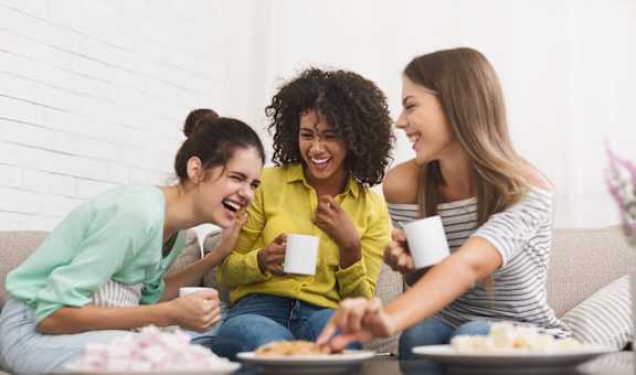 a group of women sitting on a couch eating food and drinking coffee