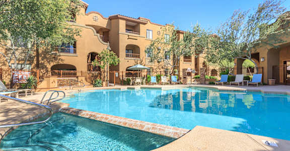 A large swimming pool in front of a building with a patio and trees.
