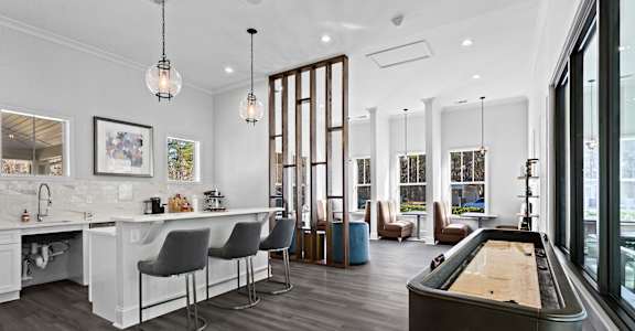 A billiard table is in the middle of a room with a bar and chairs.