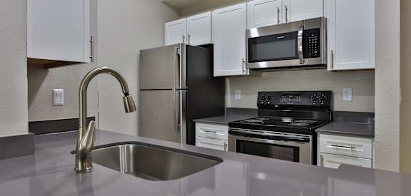 A kitchen with a stainless steel sink and black appliances. at The Quarry Alamo Heights Apartments, Texas