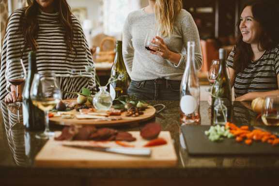 Three women are sitting at a table with food and drinks.