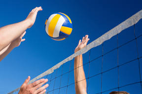 A volleyball is in the air with two hands reaching for it.