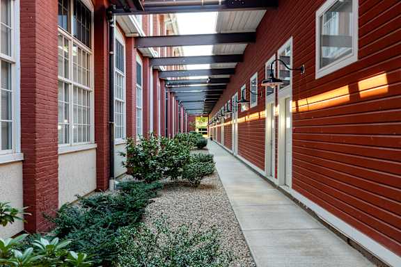 a walkway between two red brick buildings with bushes and plants