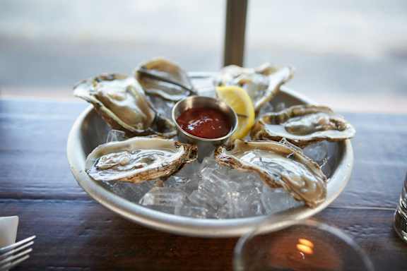 a plate of oysters on a tray of ice with a lemon and ketchup