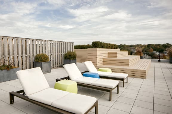 a seating area on a roof terrace with white lounge chairs and colourful ottomans