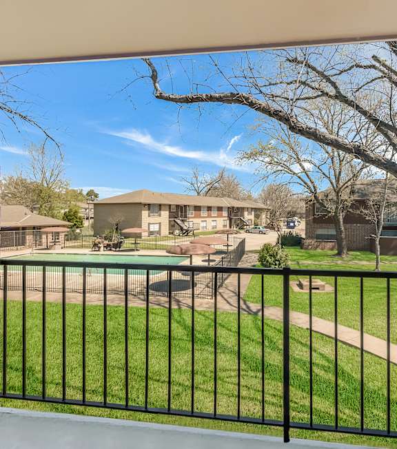 A view from a balcony looking out at a green lawn and a tree.