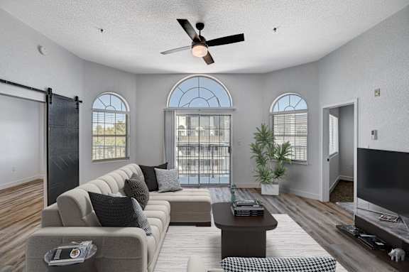 A living room with a grey sofa, a coffee table, a ceiling fan, and a sliding glass door.