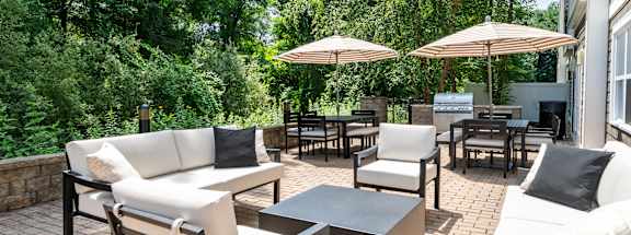 A patio with white couches, chairs, and umbrellas surrounded by trees.