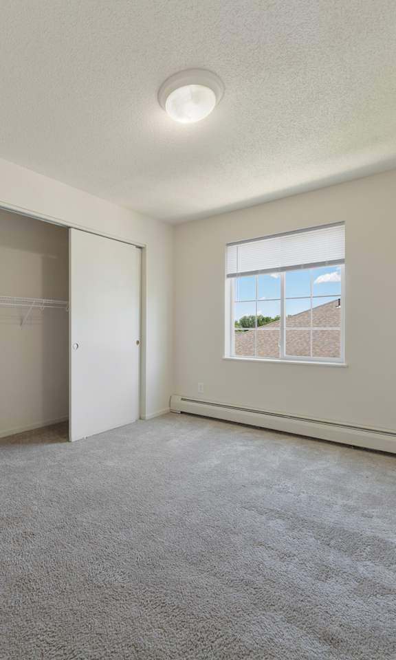 A spacious room with a carpeted floor and a window showing a building outside.