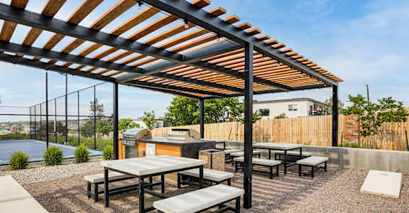 a patio with tables and benches and a barbecue grill
