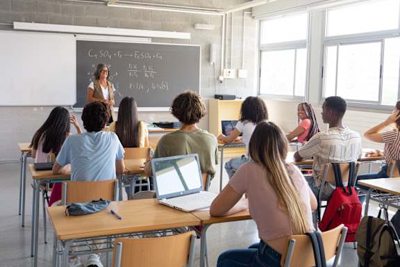 A person is writing on a paper with a pen in a classroom.