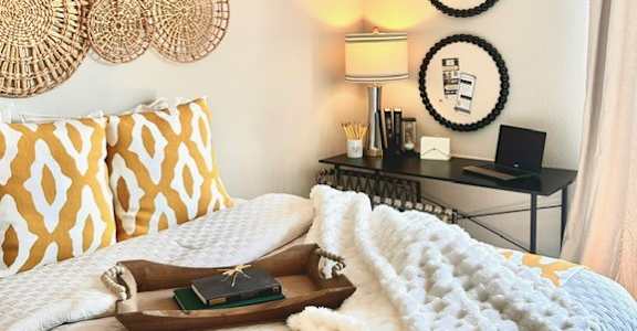 A bedroom with a bed covered in a white and gold comforter and a black desk with a laptop on it.