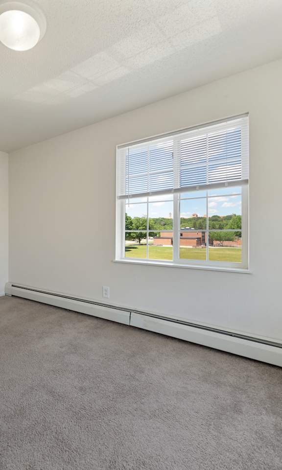 A room with a window showing a view of a building and trees outside.
