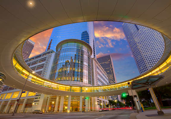 A modern building with a curved glass facade is illuminated at dusk.