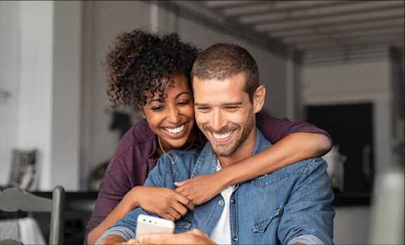 A man and woman are embracing each other while looking at a smartphone.