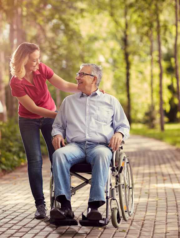 A woman pushing a man in a wheelchair through a park at Union at Rivers Edge, Des Moines, IA