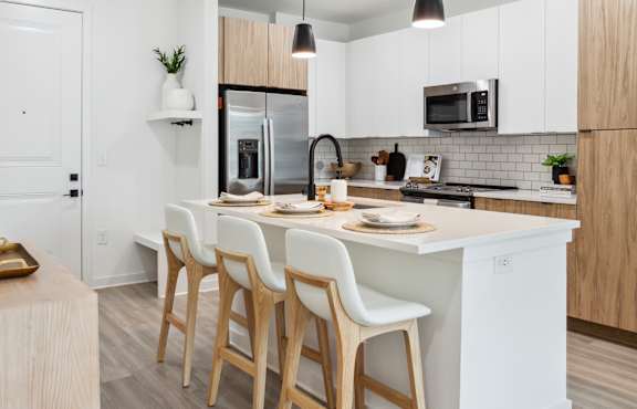 A modern kitchen with a white island and wooden chairs.