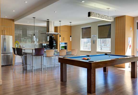 A pool table is in the middle of a room with a kitchen in the background.