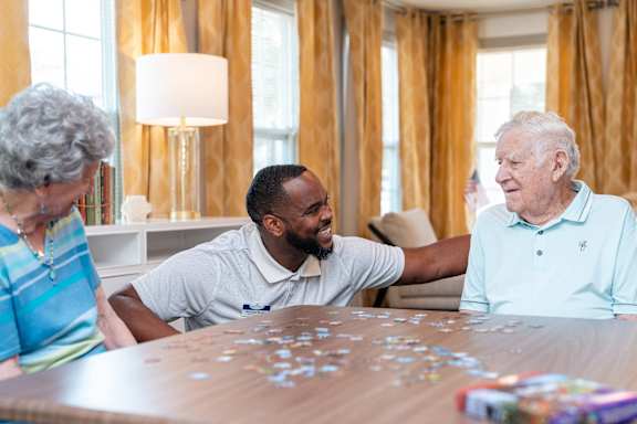 Three people sitting around a table playing with puzzle pieces.