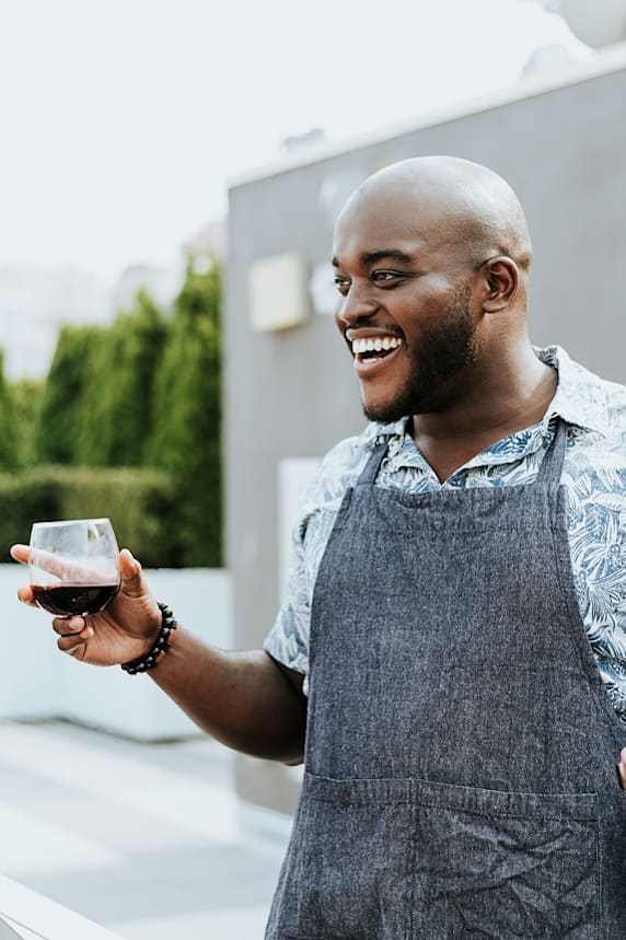 A man in a grey apron holds a glass of red wine.