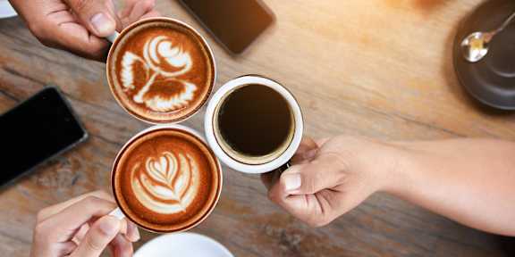 Three cups of coffee with latte art designs being held by people.