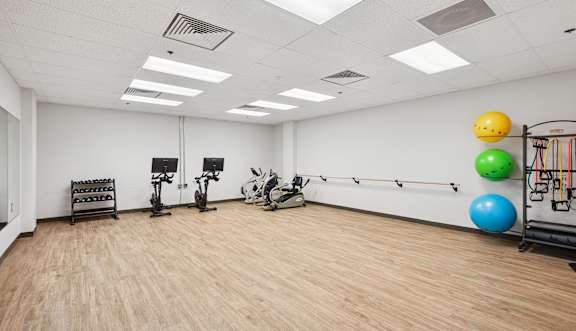 A gym with exercise equipment and a wall of windows.
