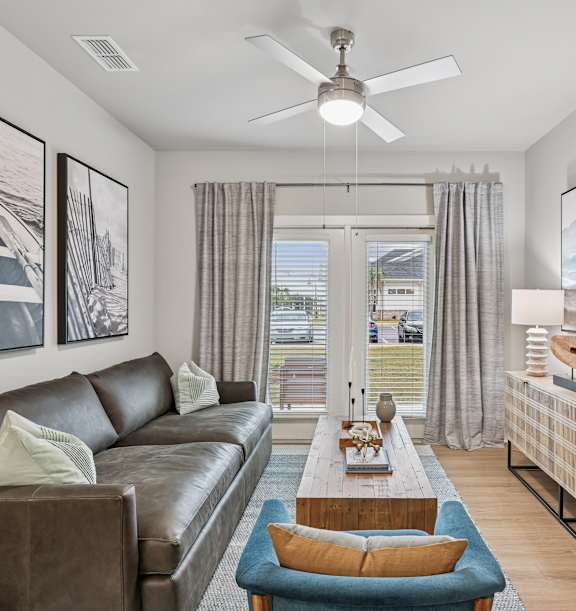 a family sitting on a couch smiling and waving to the camera at The Exchange at Crestview Apartments, Crestview, FL, 32536