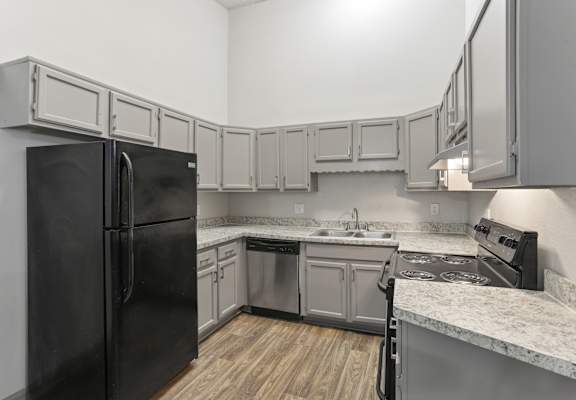 A black refrigerator is in a kitchen with wooden floors and marble countertops.
