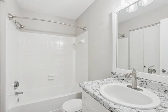 A white bathroom with a marble countertop and a white toilet.
