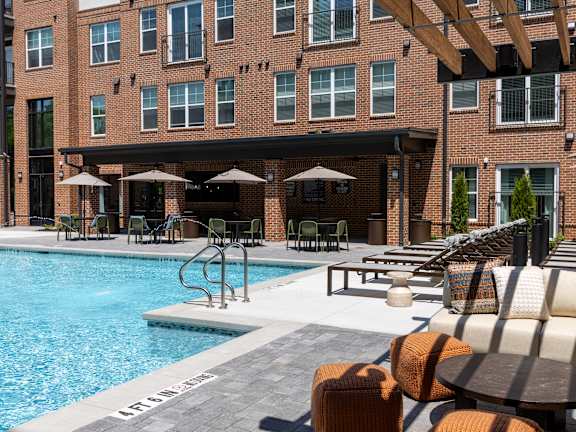 A pool surrounded by a patio with lounge chairs and umbrellas at District on the Etowah Apartments, Canton, 30114