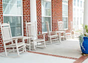 Thumbnail 2 of 17 - A row of white rocking chairs are lined up on a porch.