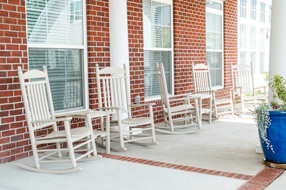 A row of white rocking chairs are lined up on a porch.