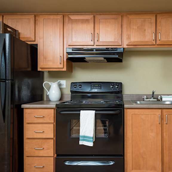 Apartment kitchen with wood cabinets and black appliances at Monroe Street Apartments