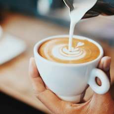 A person is pouring milk into a cup of coffee.