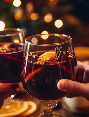 two hands holding glasses of red wine in front of a christmas tree